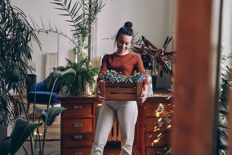 a woman standing with a box of plants